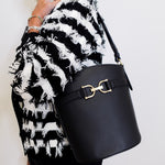 Person wearing a black and white patterned coat holding a black handbag with a gold clasp.