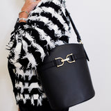 Person wearing a black and white patterned coat holding a black handbag with a gold clasp.