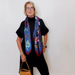 Woman wearing a colorful scarf and holding a brown handbag against a white wall.