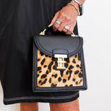 Person holding a black handbag with leopard print panel against a plain background
