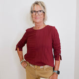 Woman wearing a burgundy top and beige pants against a white background