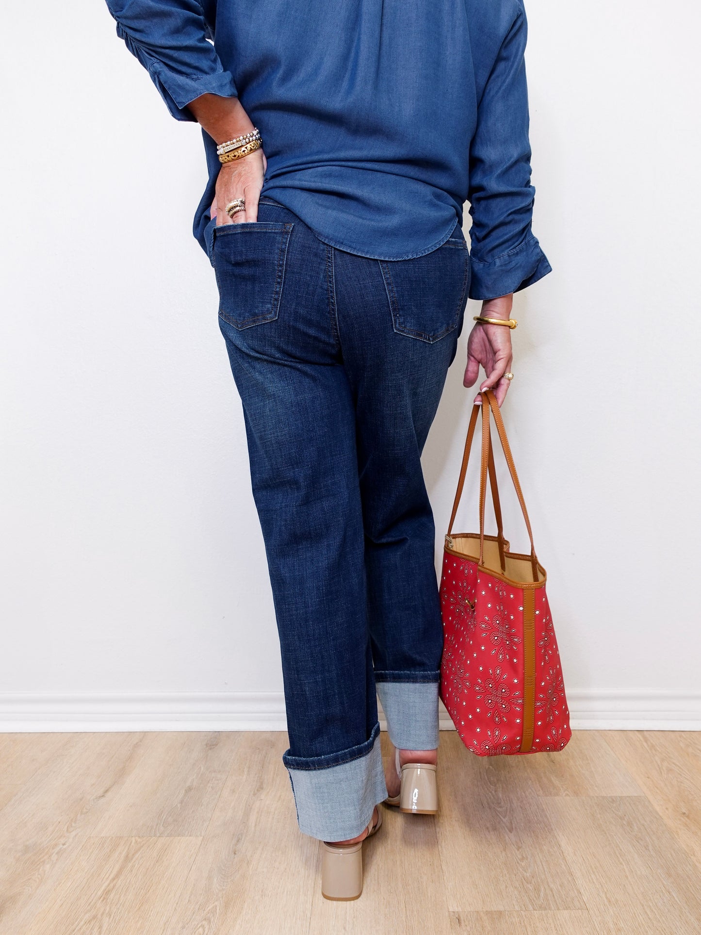 Person wearing blue jeans and a blue top, holding a red patterned bag on a light wooden floor.