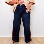 Person wearing a beige shirt and dark blue jeans with a white wall background