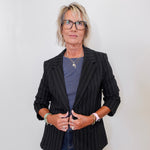 Person wearing a black pinstripe blazer over a blue shirt with a plain background