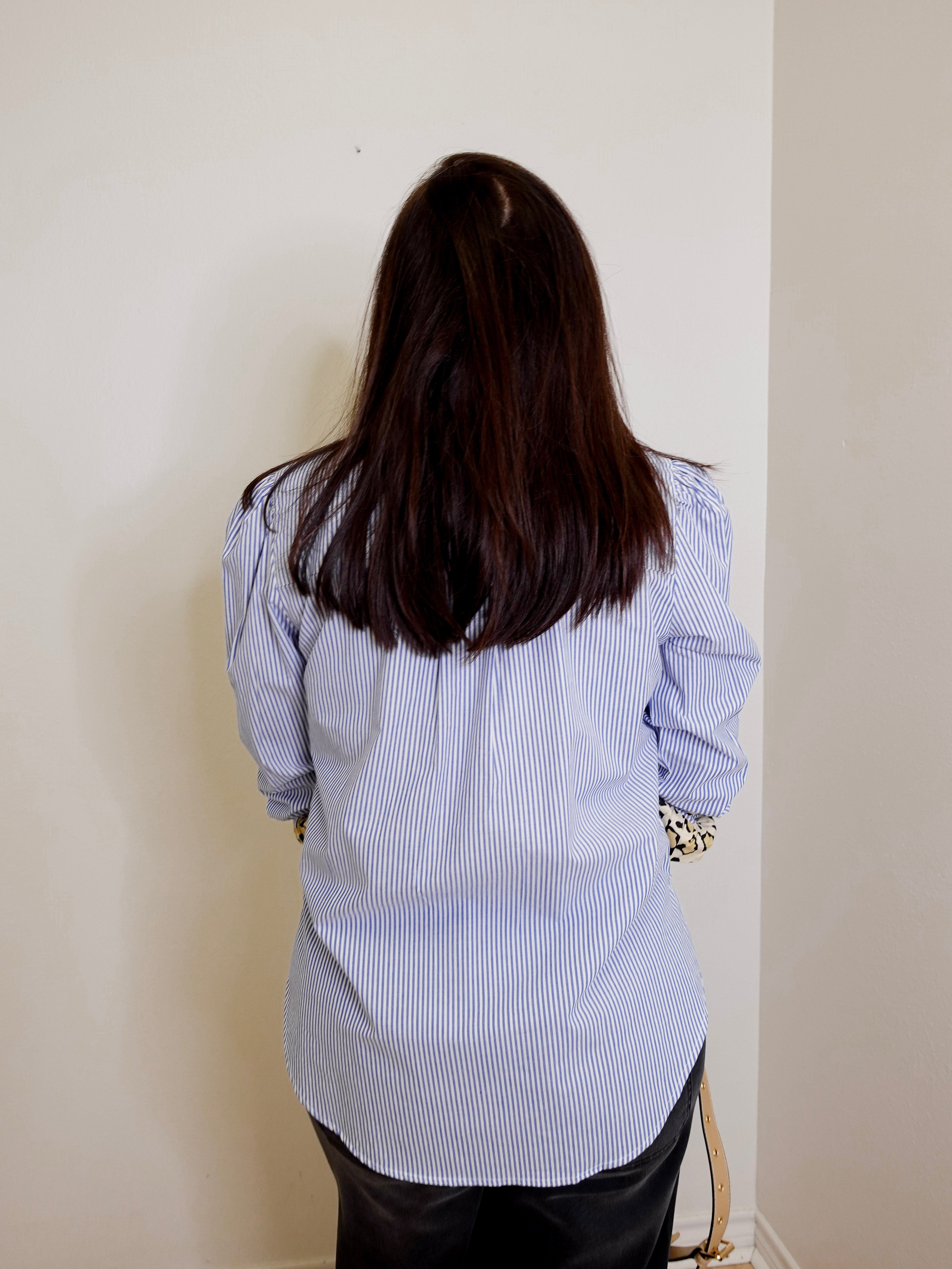Person wearing a blue and white striped shirt against a plain wall.