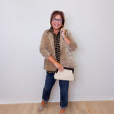 Woman wearing a beige cardigan, blue jeans, and holding a white clutch against a white wall.