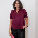 Woman wearing a burgundy blouse and black pants, holding a pink clutch against a white background