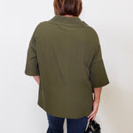 Person wearing an olive green jacket and dark blue jeans, holding a black handbag against a white background