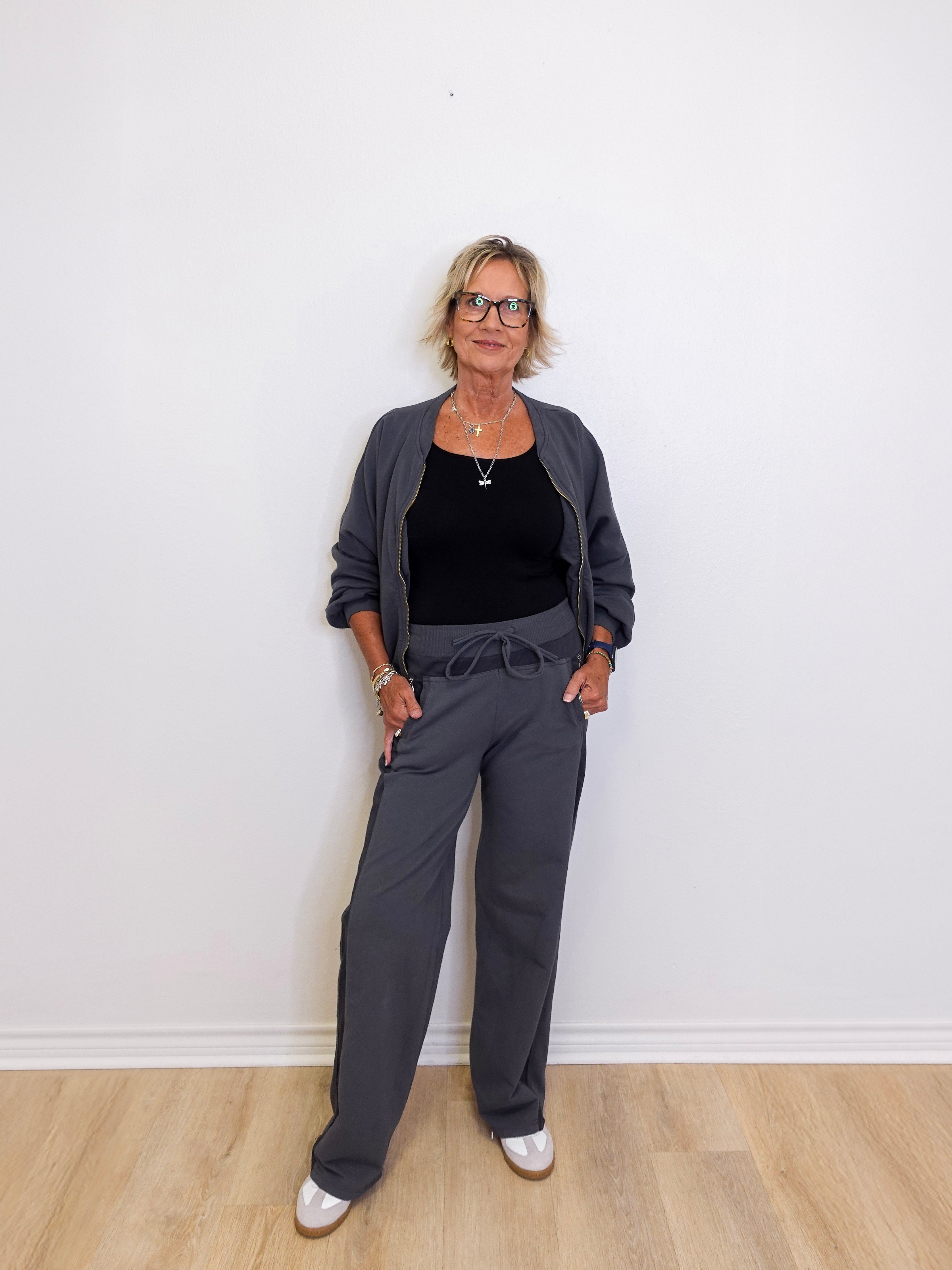 Woman wearing a gray outfit standing against a white wall.