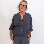 Woman wearing a gray bomber jacket and pants against a white background