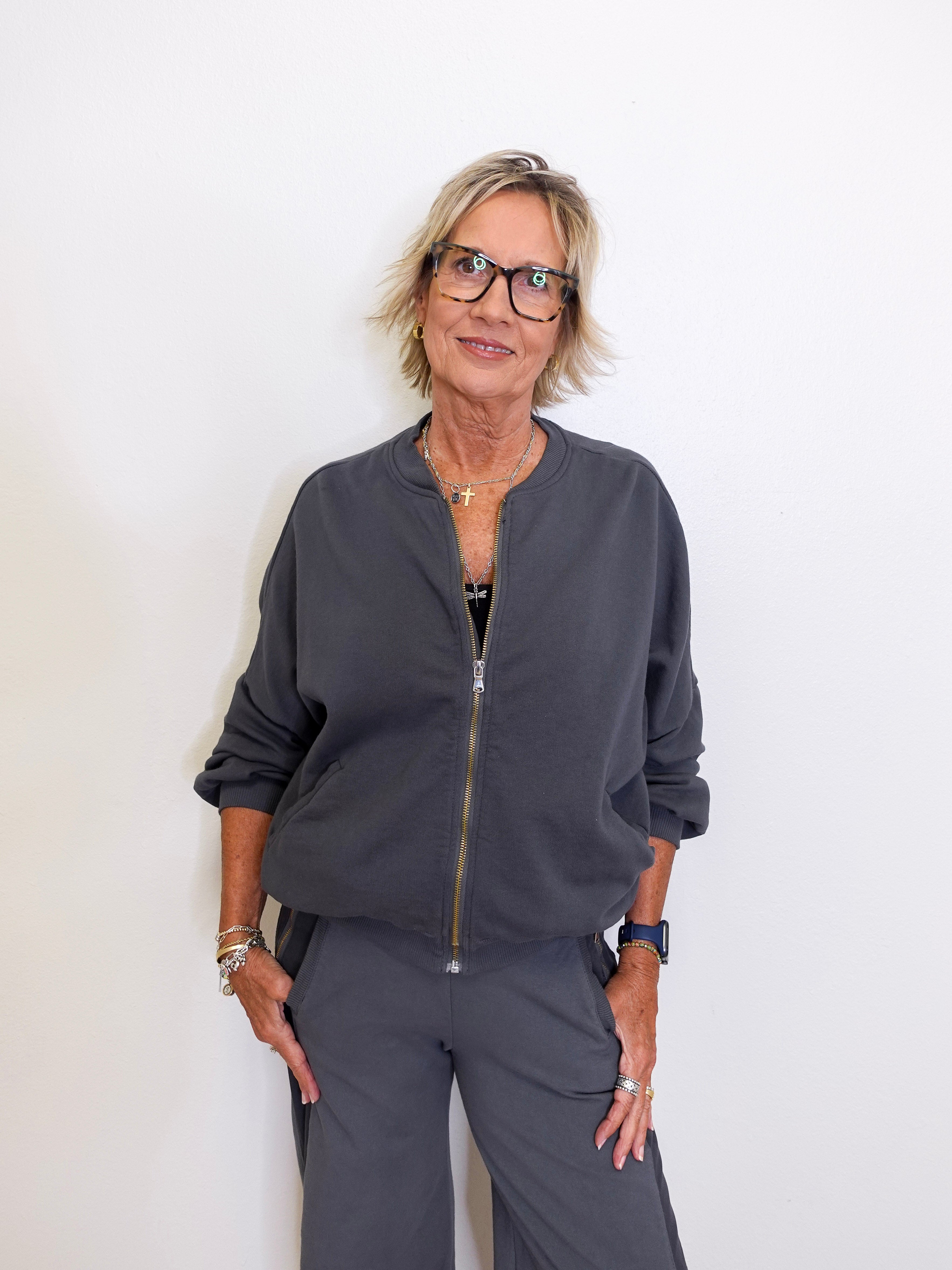 Woman wearing a gray bomber jacket and pants against a white background