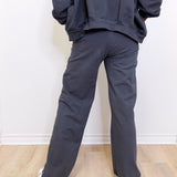 Person wearing a dark gray hoodie and pants standing against a white wall.