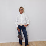 Person wearing a white shirt, dark jeans, and brown shoes against a plain white wall.