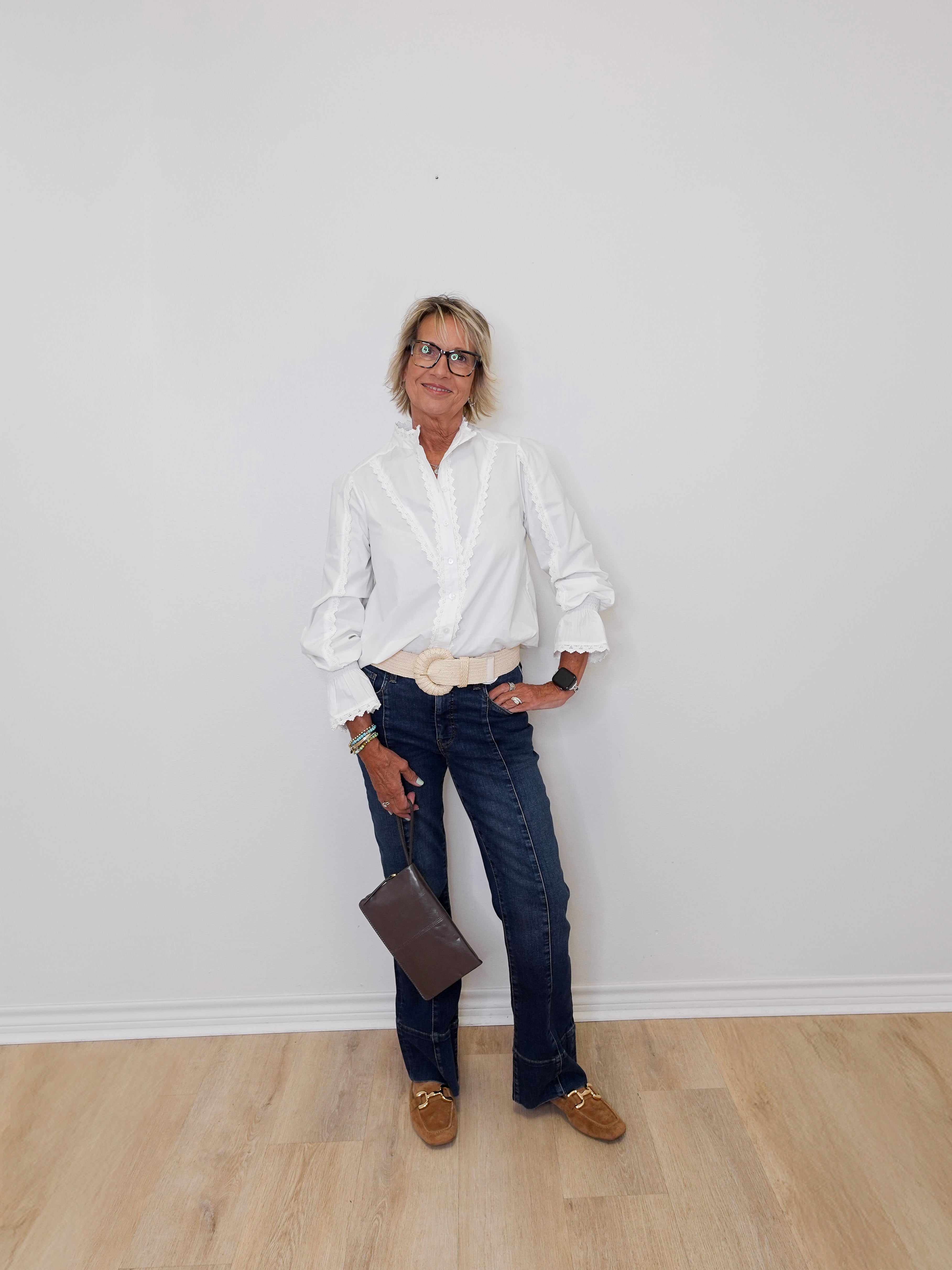 Person wearing a white shirt, dark jeans, and brown shoes against a plain white wall.