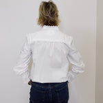 Person wearing a white blouse and dark jeans against a plain background