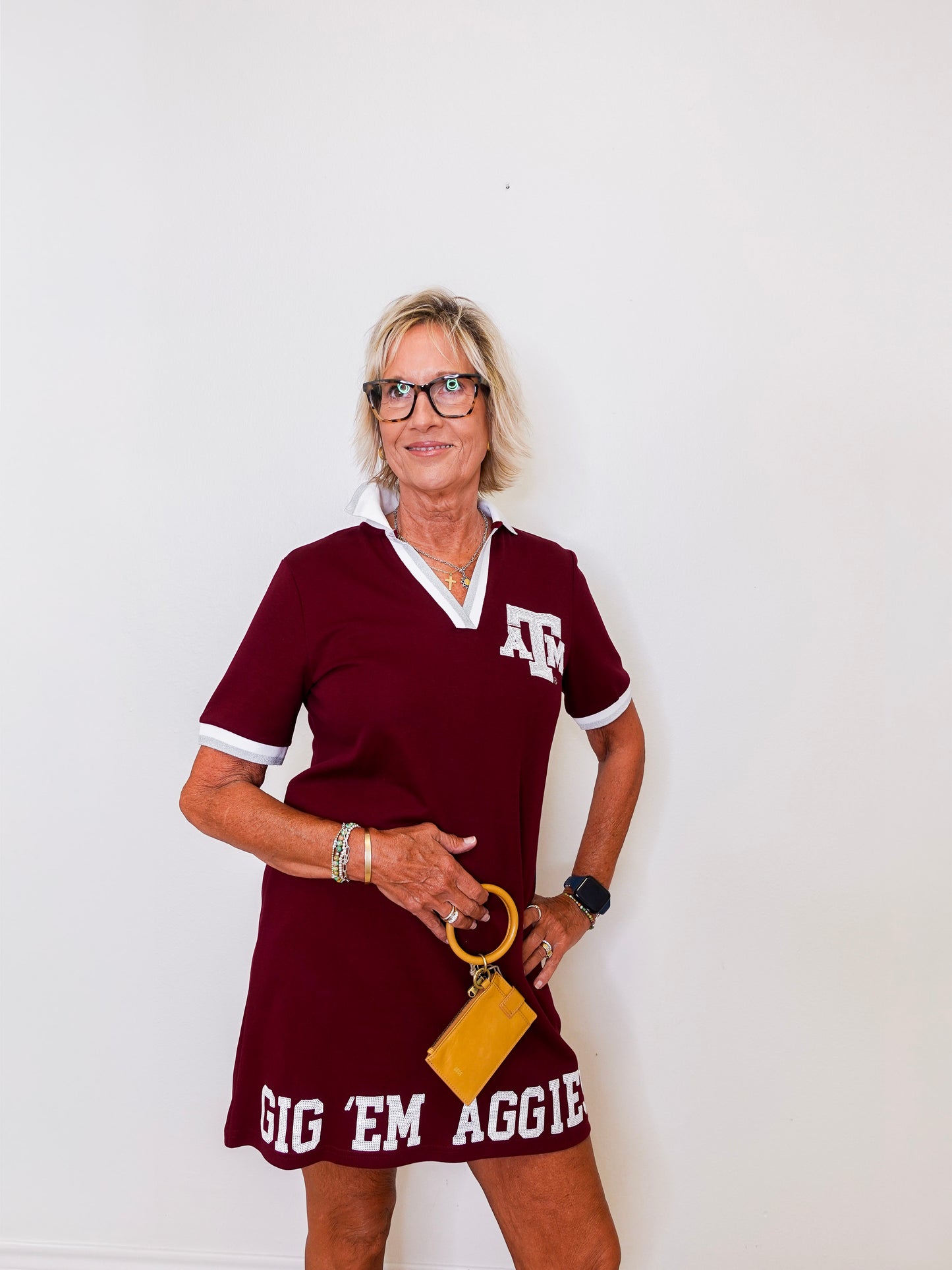 Woman wearing a maroon dress with 'Gig 'Em Aggie' text and a yellow clutch against a white background