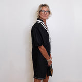 Person wearing a black dress with white trim against a plain background