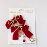 Red bow charm with gold accents and a heart detail on a white card packaging.