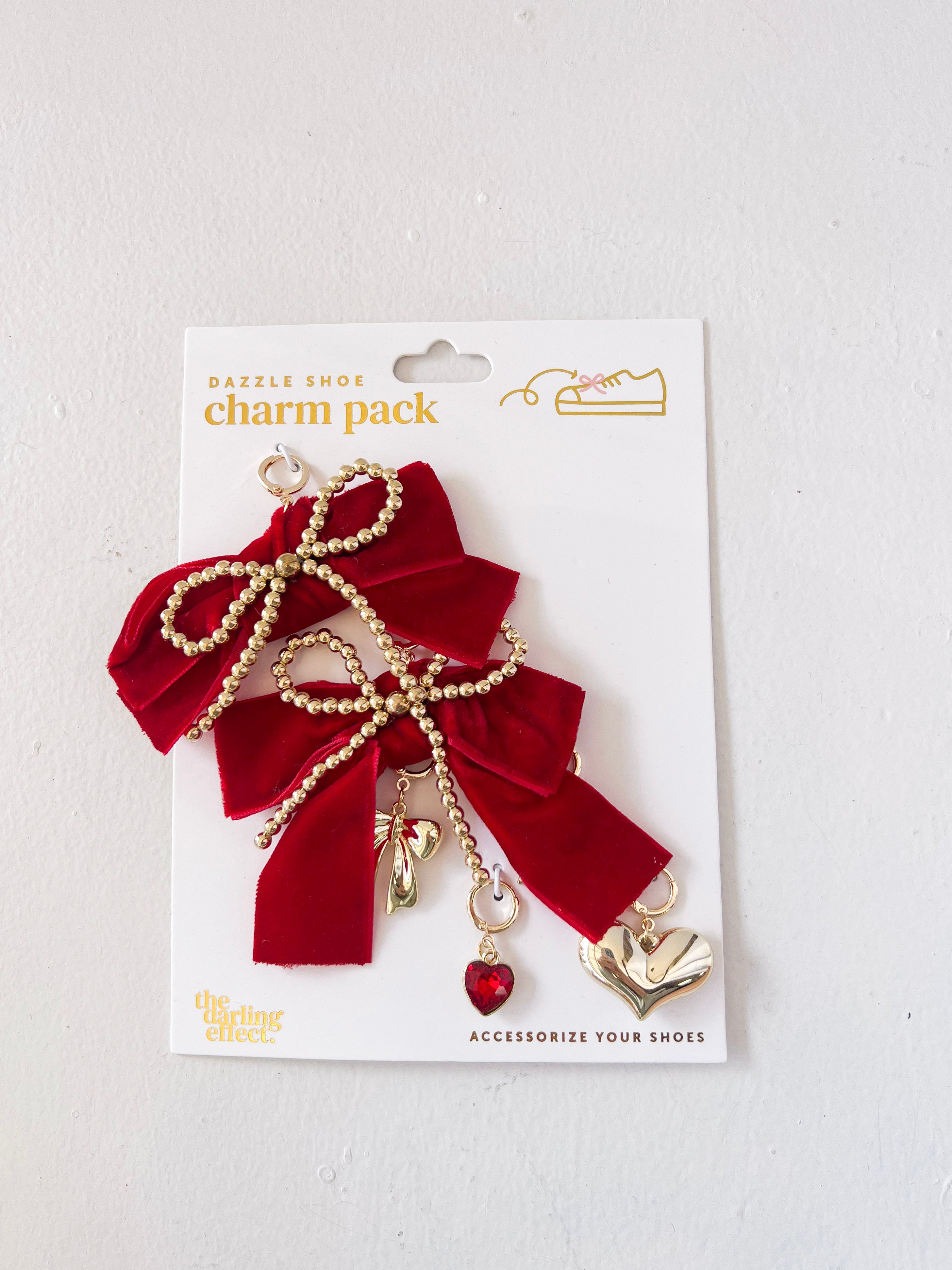 Red bow charm with gold accents and a heart detail on a white card packaging.