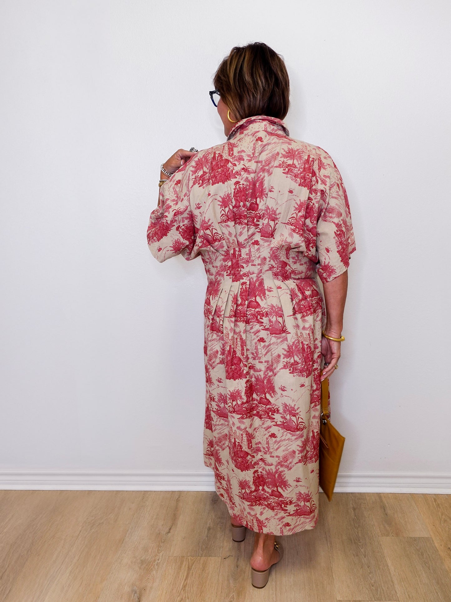 Woman wearing a red and white floral dress against a white wall.