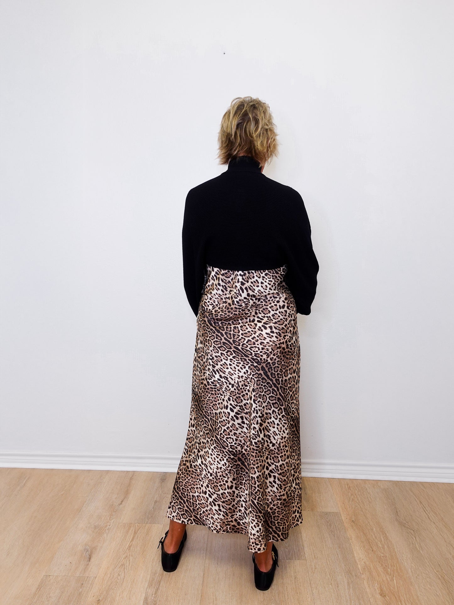 Person wearing a black top and leopard print skirt against a white wall.