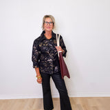 Woman in a black floral shirt and black pants holding a red bag against a white wall.