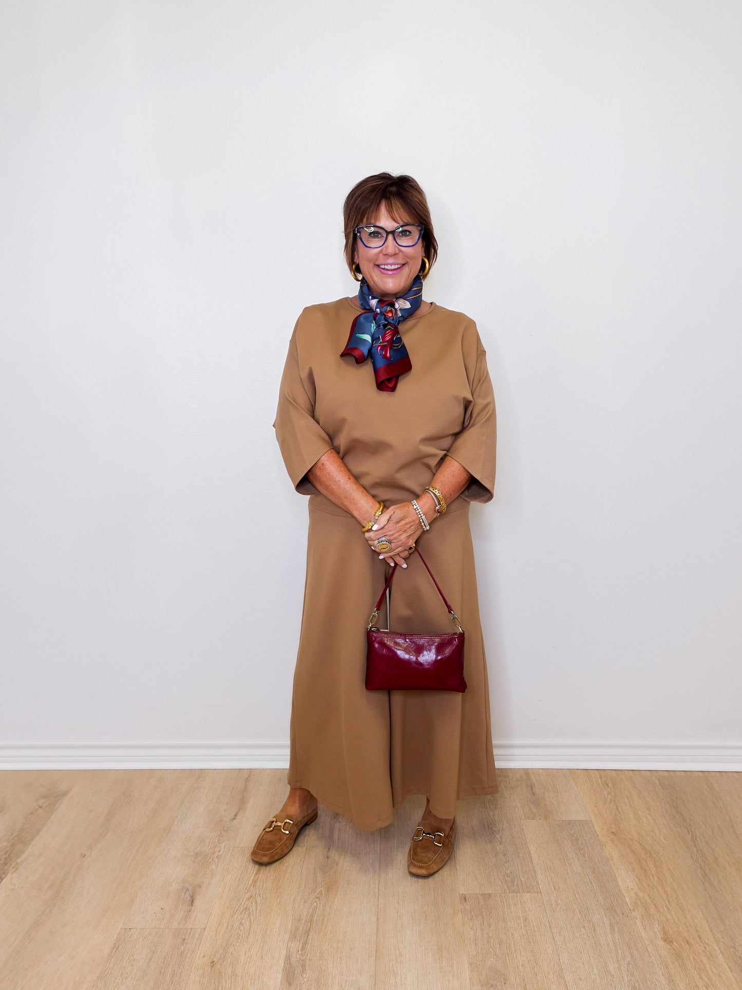 Woman in a beige dress with a red handbag against a white wall