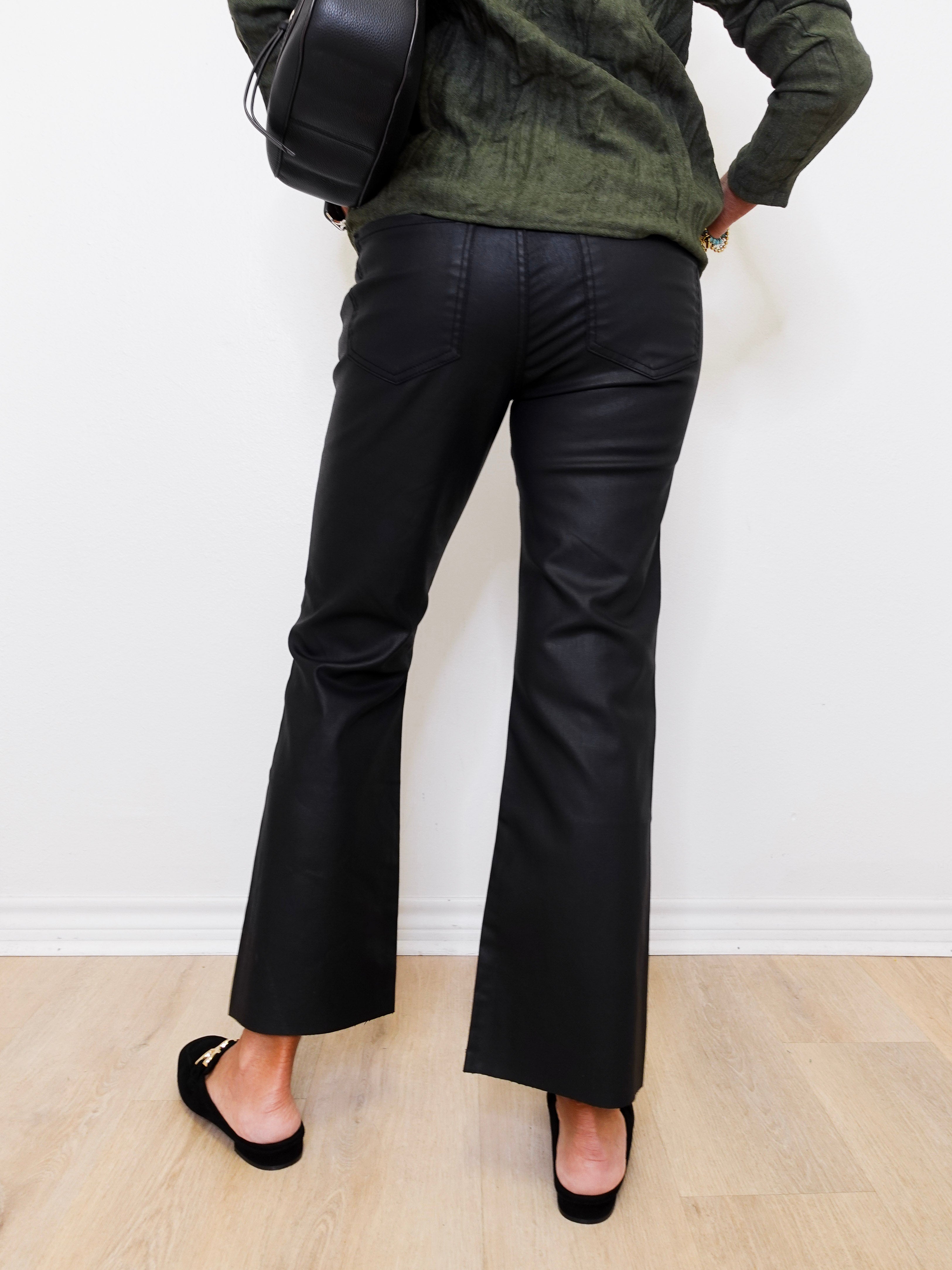 Person wearing black wide-leg pants and a green sweater against a white wall.