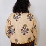 Person wearing a beige embroidered jacket with floral patterns on a plain background