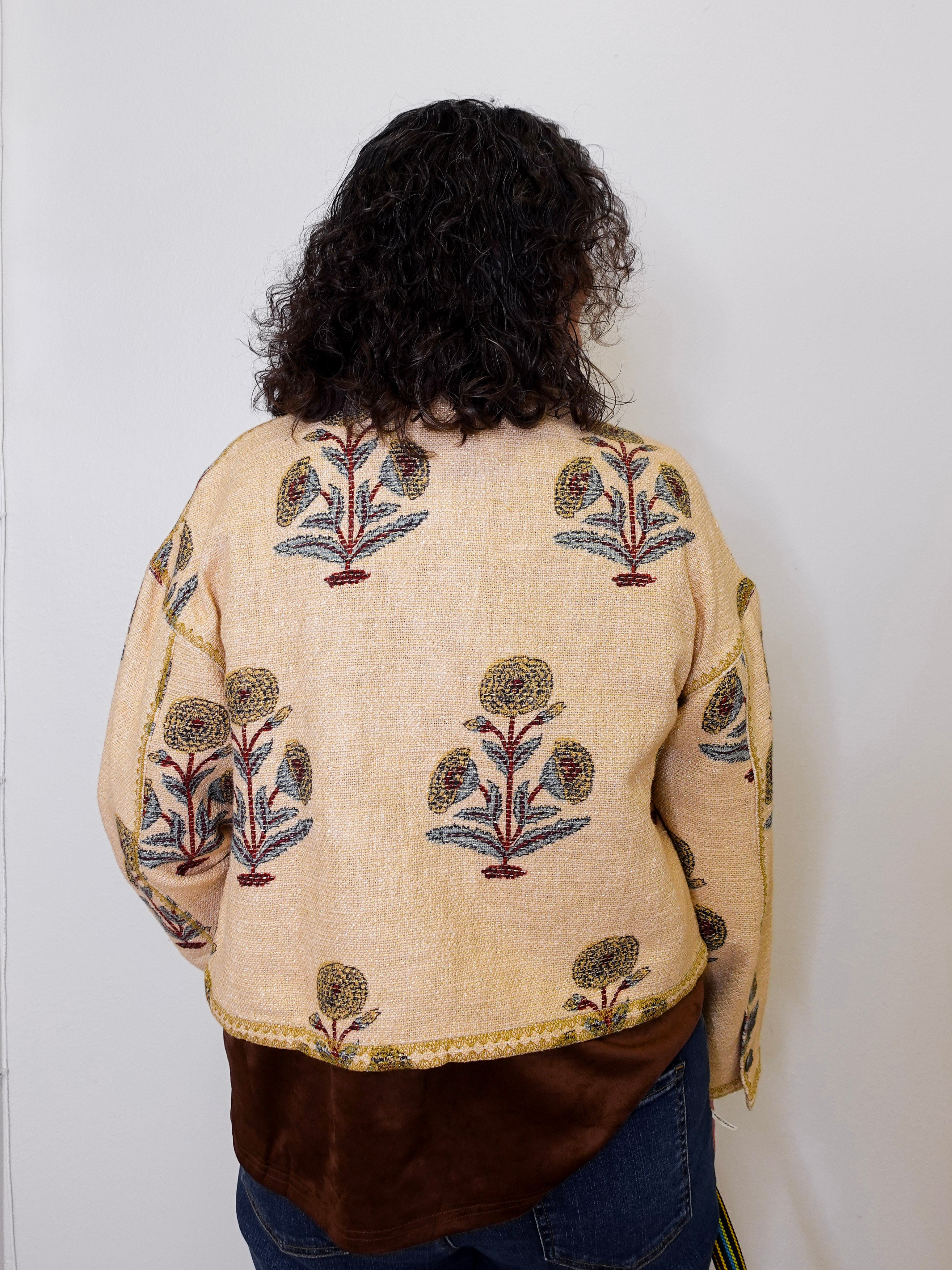 Person wearing a beige embroidered jacket with floral patterns on a plain background