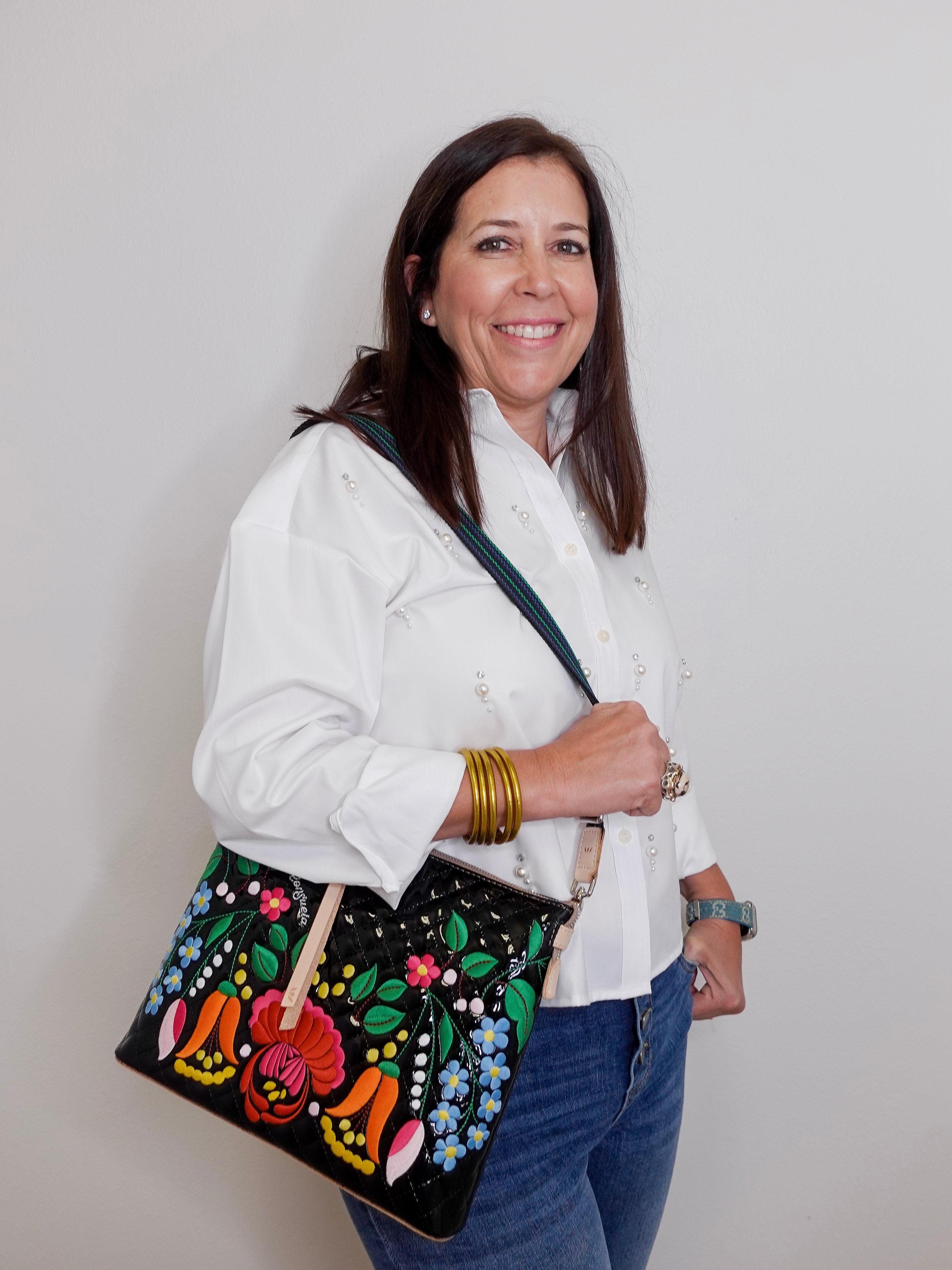 Woman holding a black handbag with colorful floral embroidery against a plain background