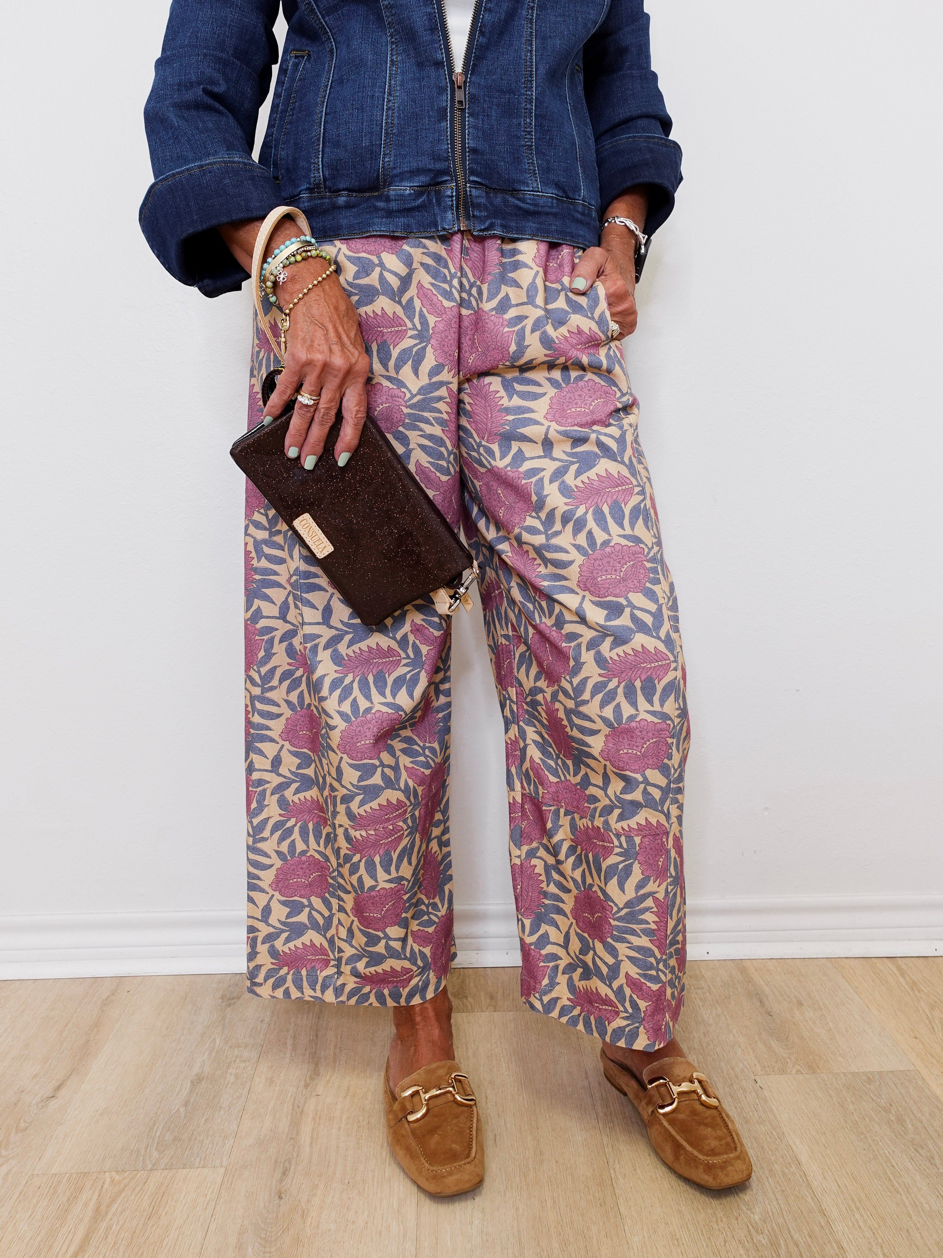 Person wearing a denim jacket, patterned pants, and brown loafers against a white wall.
