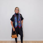 Woman wearing a colorful scarf and holding a handbag against a white wall.