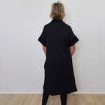 Person wearing a black dress standing against a white wall.