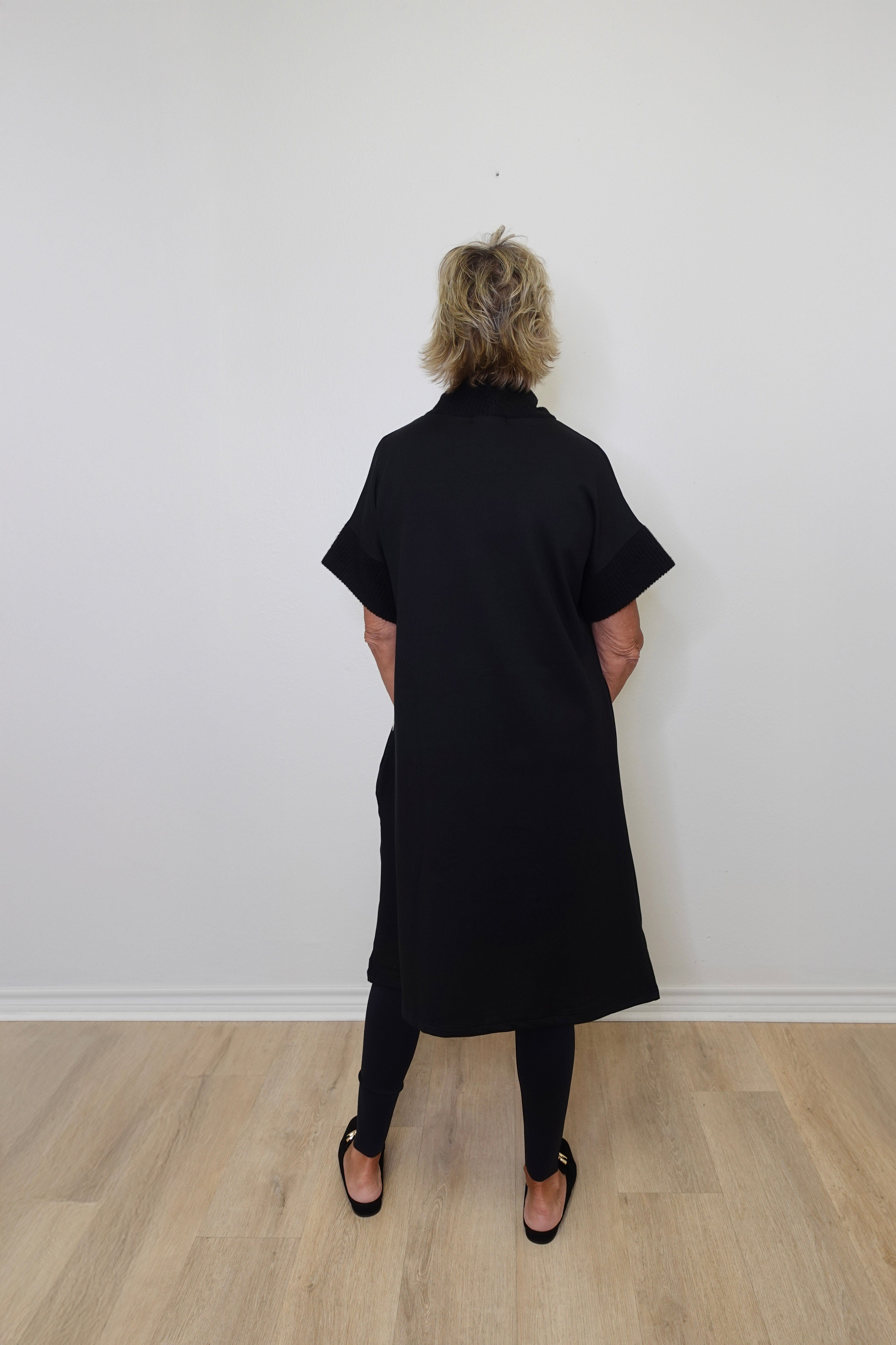 Person wearing a black dress standing against a white wall.