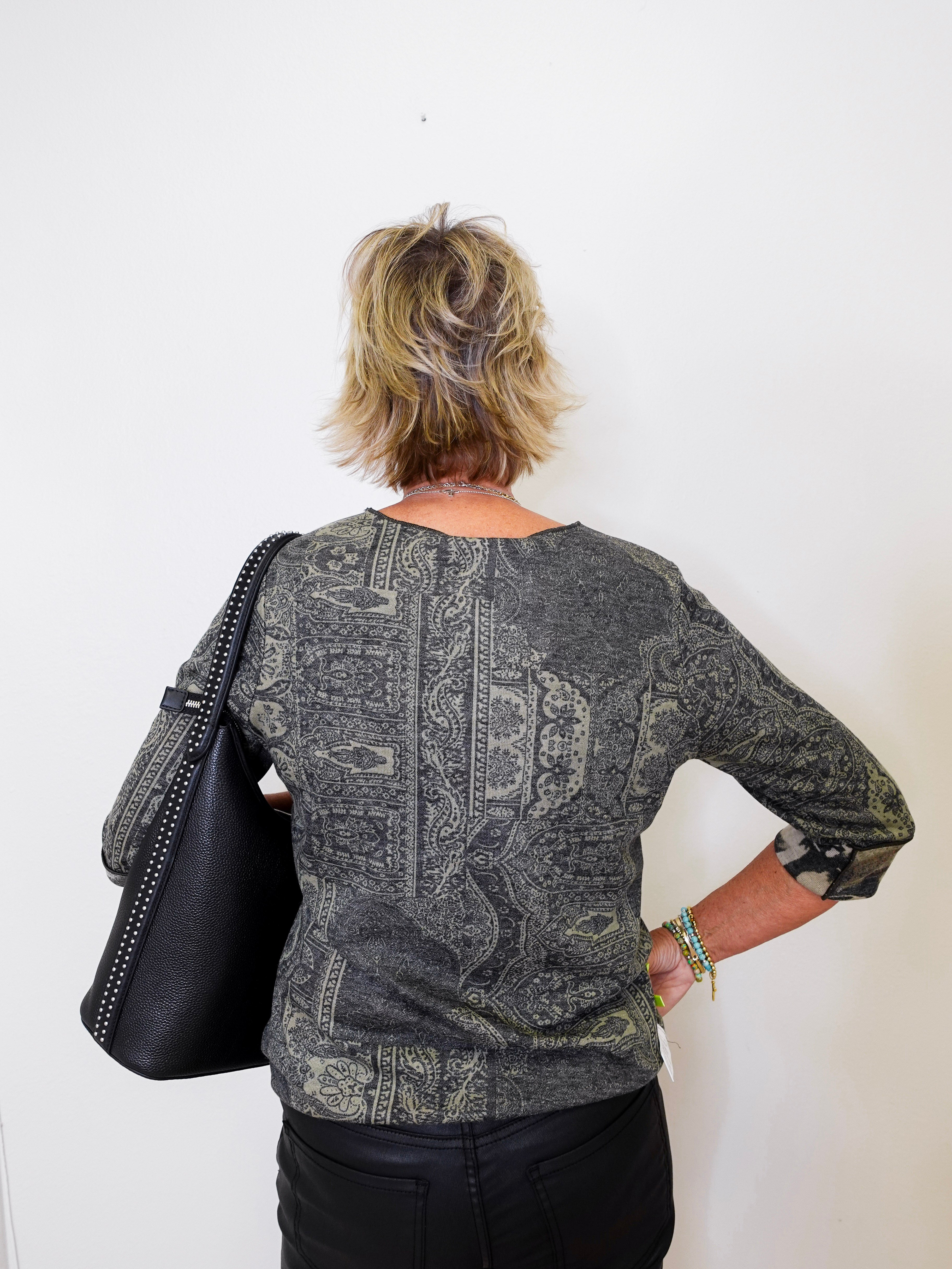 Person wearing a patterned shirt holding a black bag against a white background