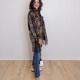Woman wearing a plaid shawl, jeans, and white sneakers against a plain background
