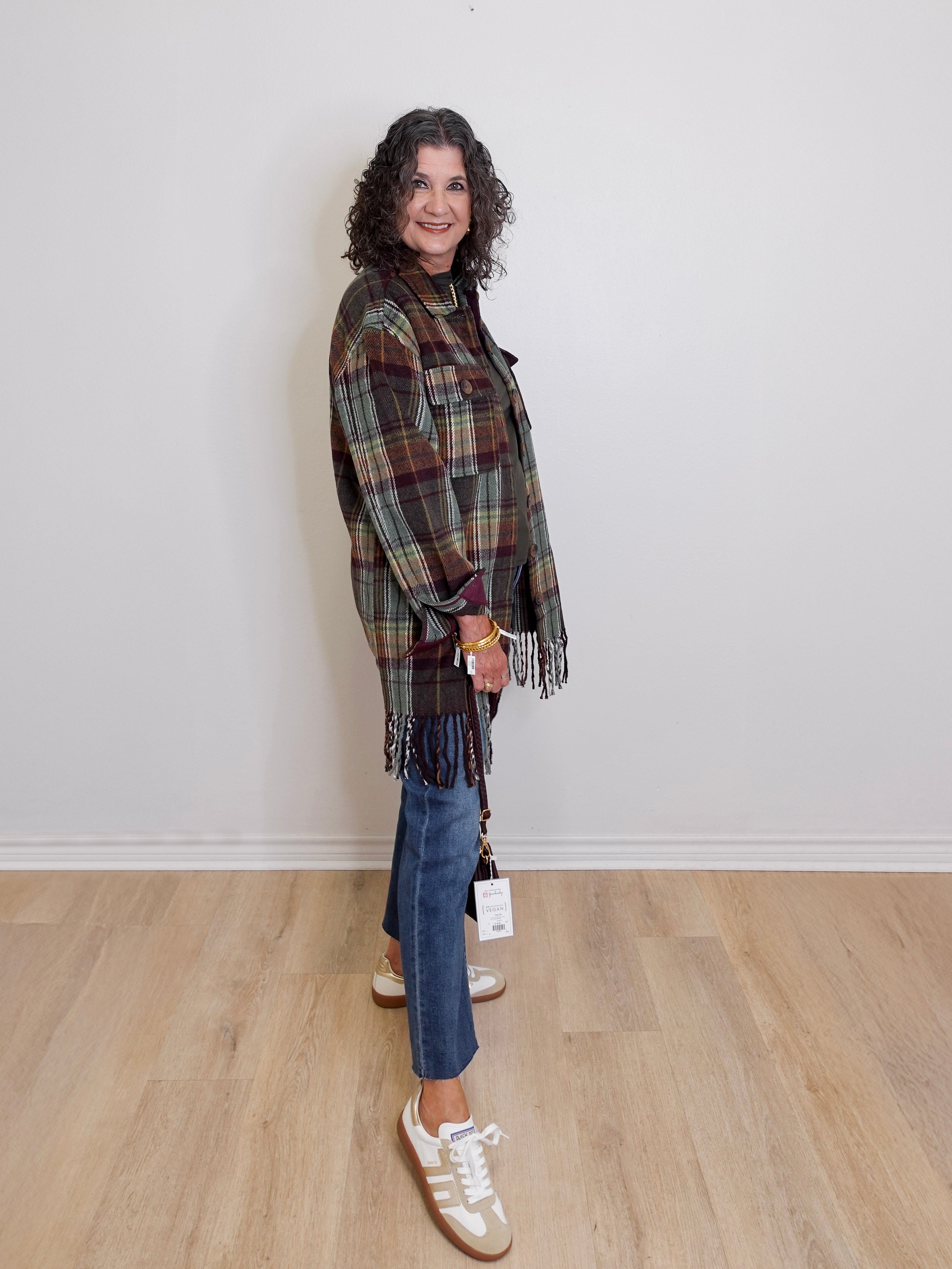 Woman wearing a plaid shawl, jeans, and white sneakers against a plain background