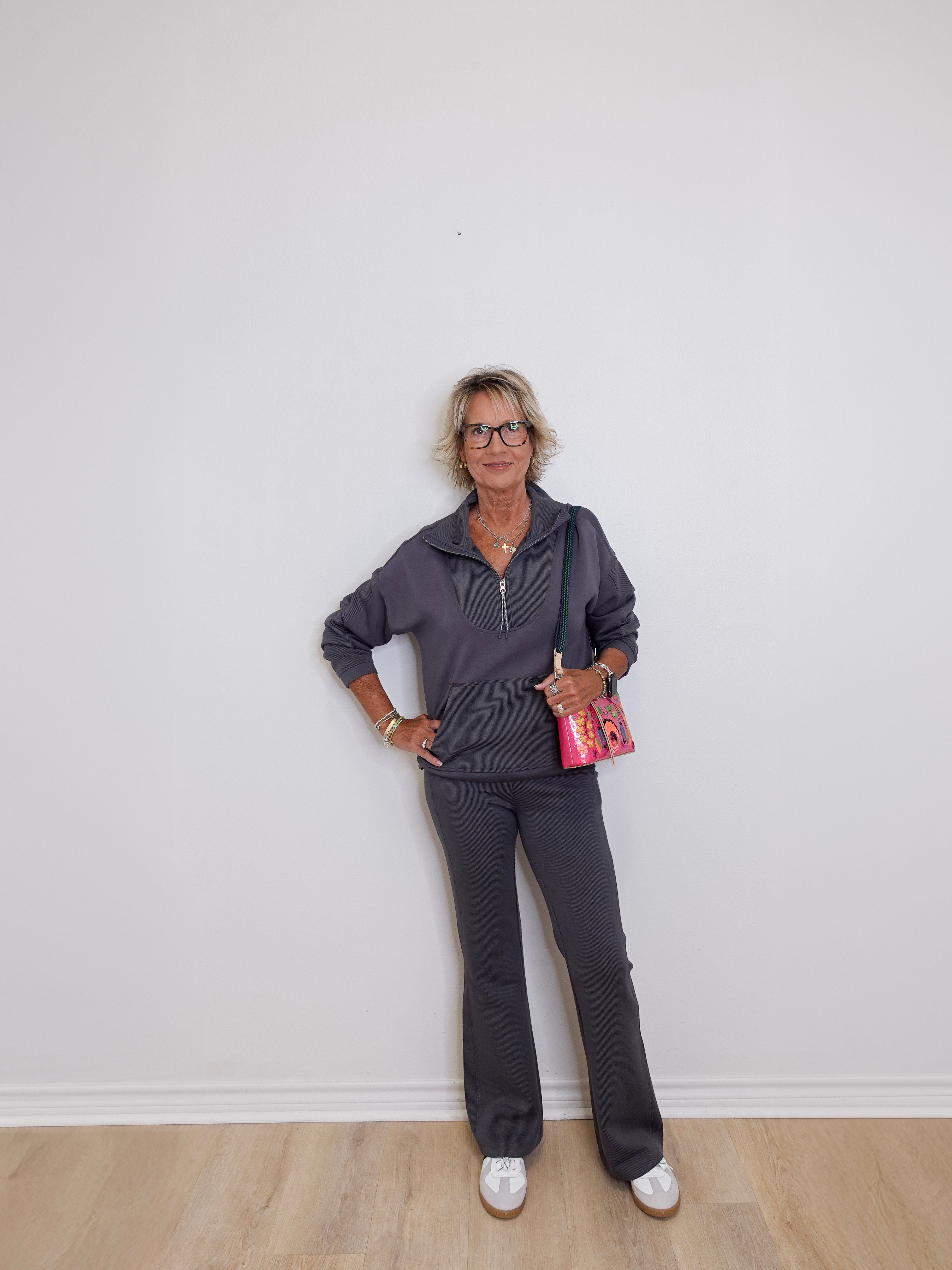 Woman in gray outfit standing against a white wall
