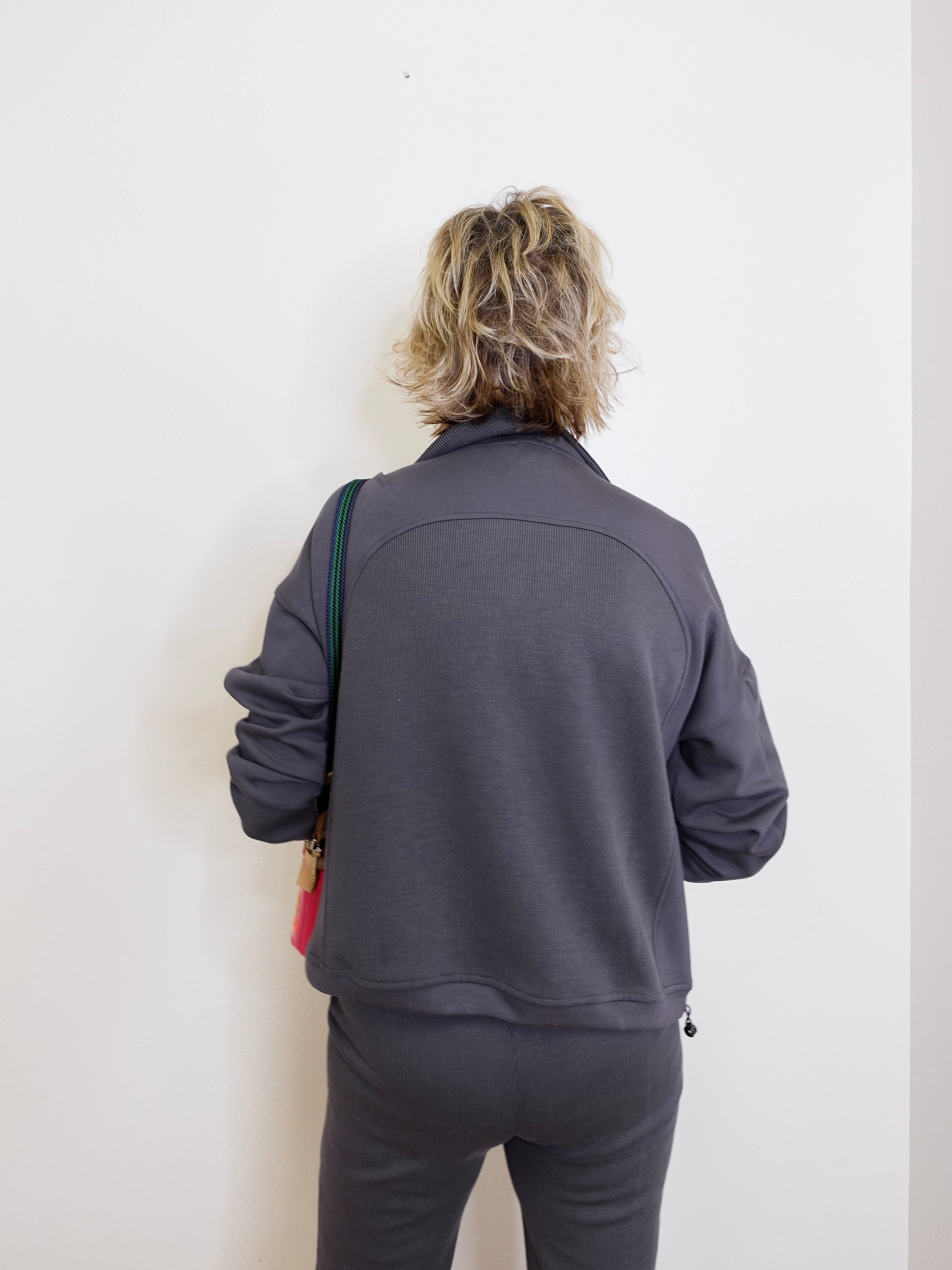 Person wearing a gray tracksuit against a white wall