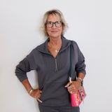 Woman wearing a gray zip-up sweatshirt and black pants against a white background