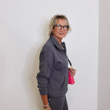 Woman in gray outfit holding a pink bag against a white wall