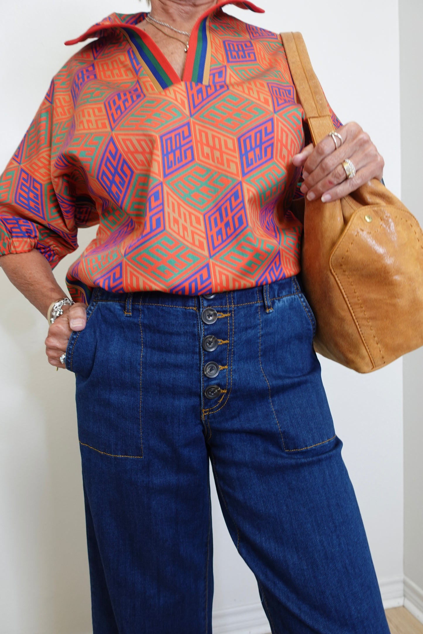Person wearing a colorful geometric patterned shirt and blue jeans, holding a brown bag.