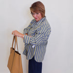 Woman in a striped shirt holding a tan handbag against a white wall