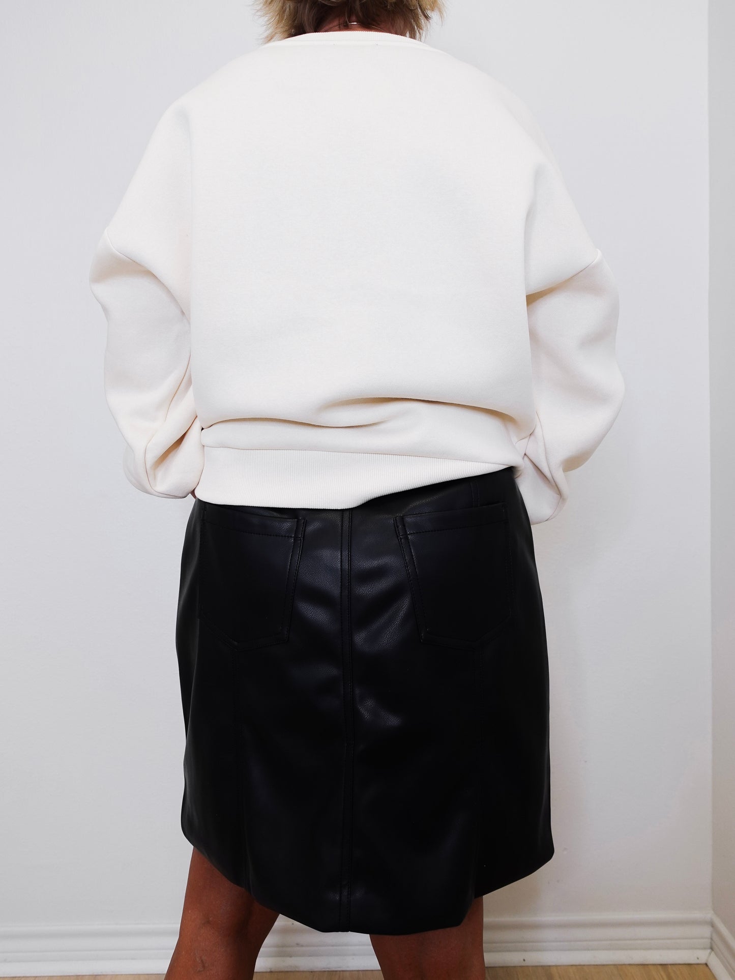 Person wearing a white sweater and black leather skirt against a plain background