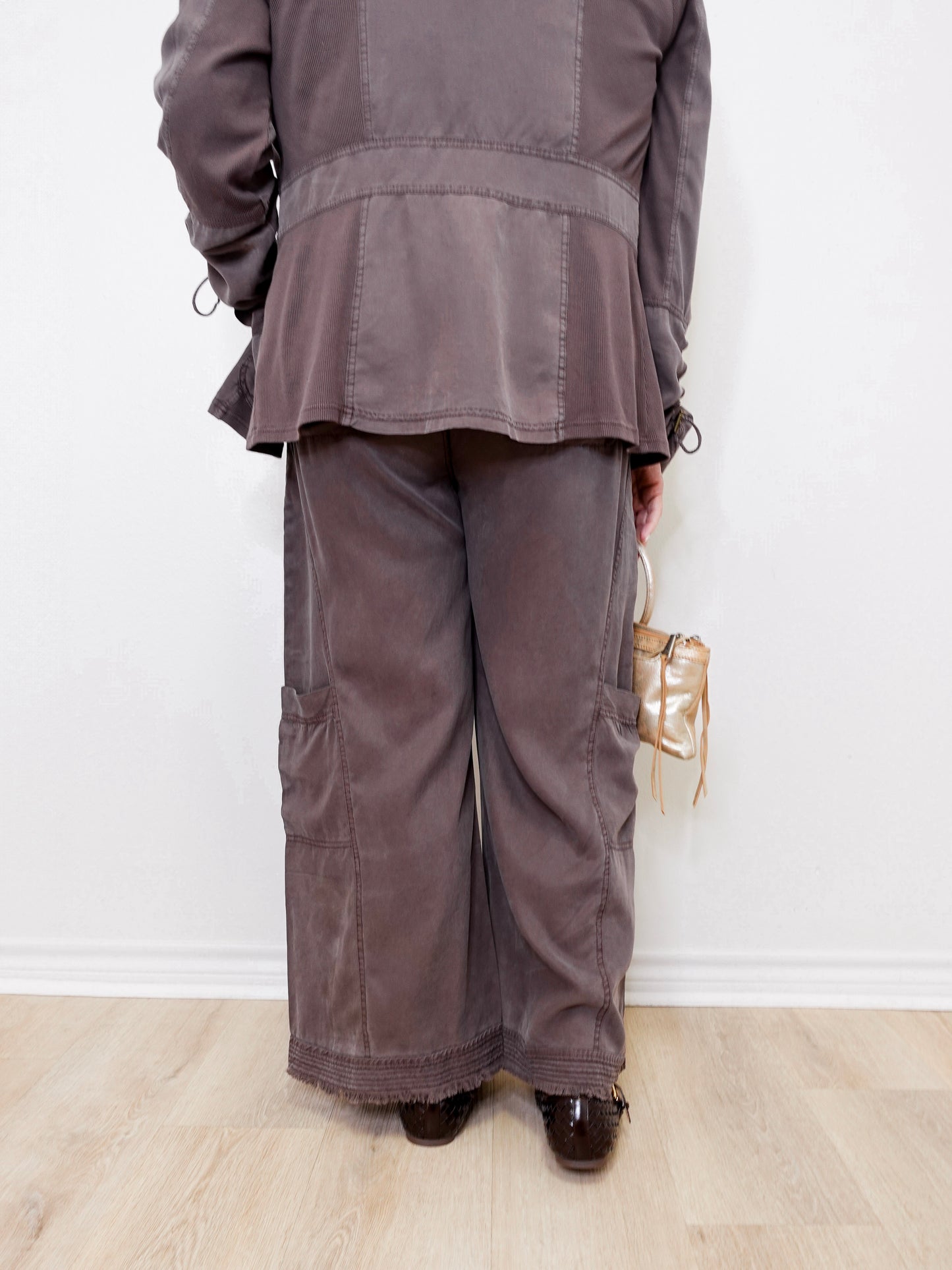 Person wearing a gray outfit with wide-leg pants against a white wall.