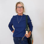 Woman wearing a blue top and jeans, holding a bag against a white background