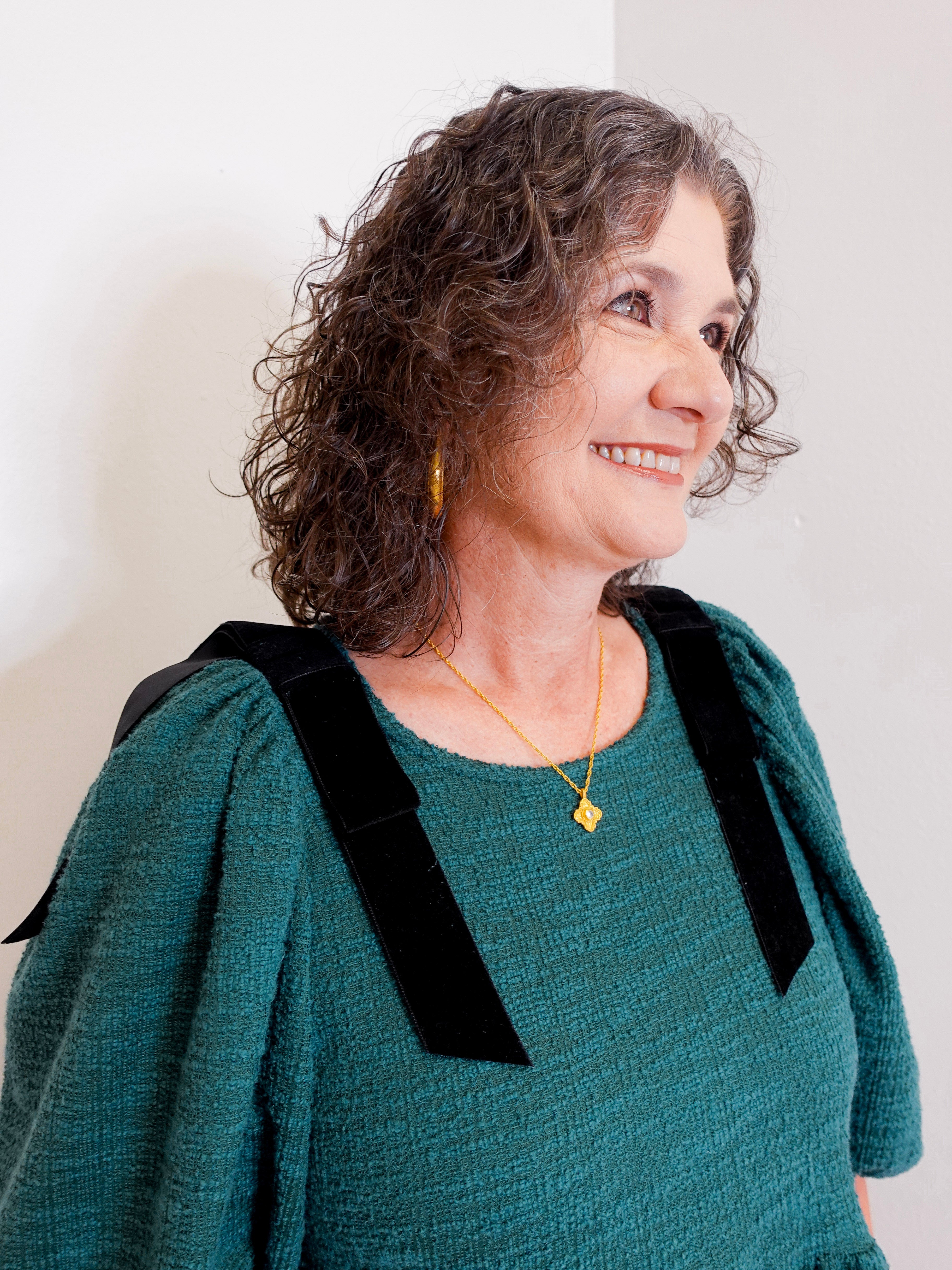 Woman wearing a green dress with black shoulder accents against a plain background