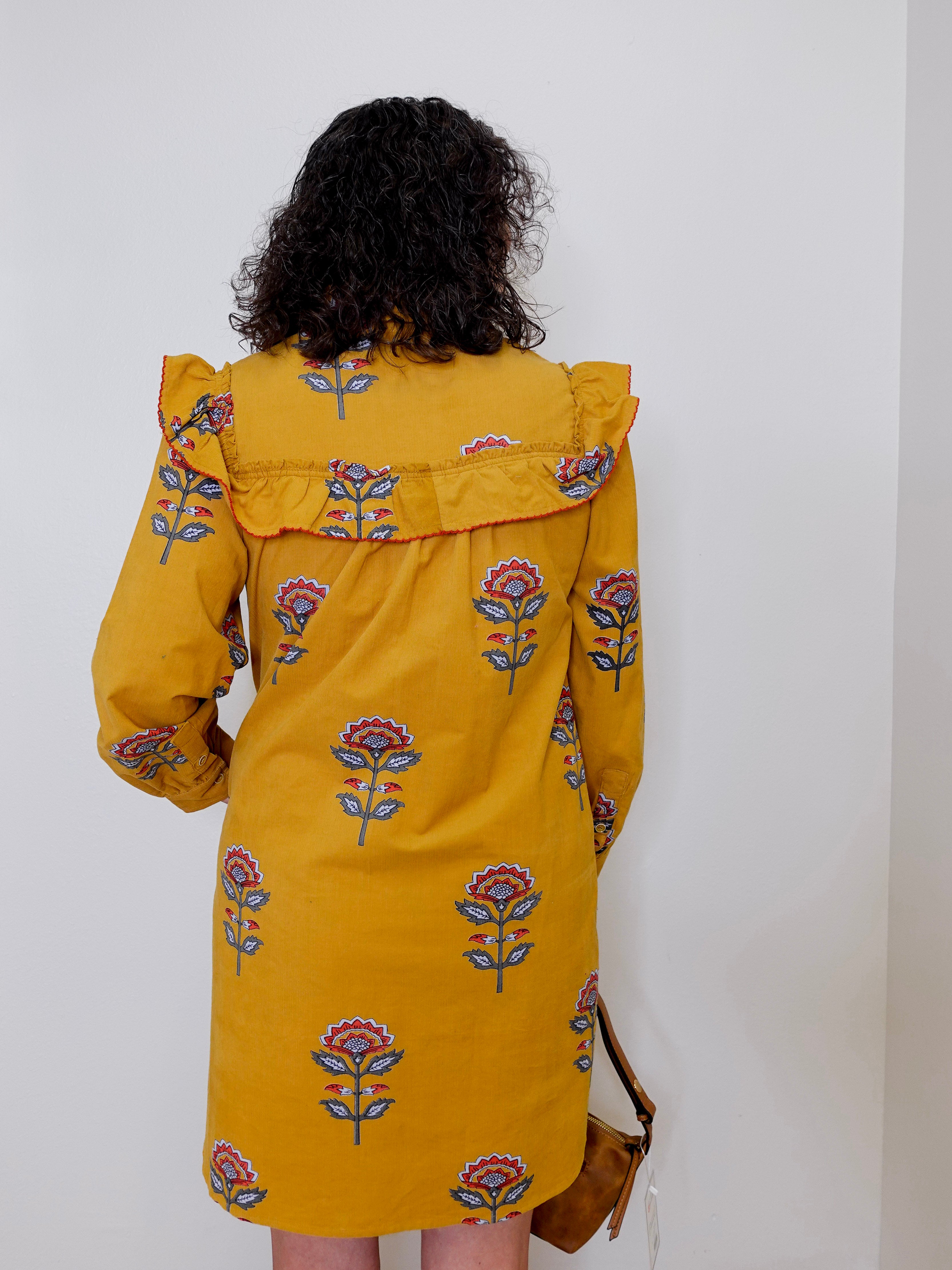 Person wearing a yellow dress with floral patterns against a white background