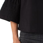 Close-up of a person wearing a black blouse with smocked sleeves on a white background